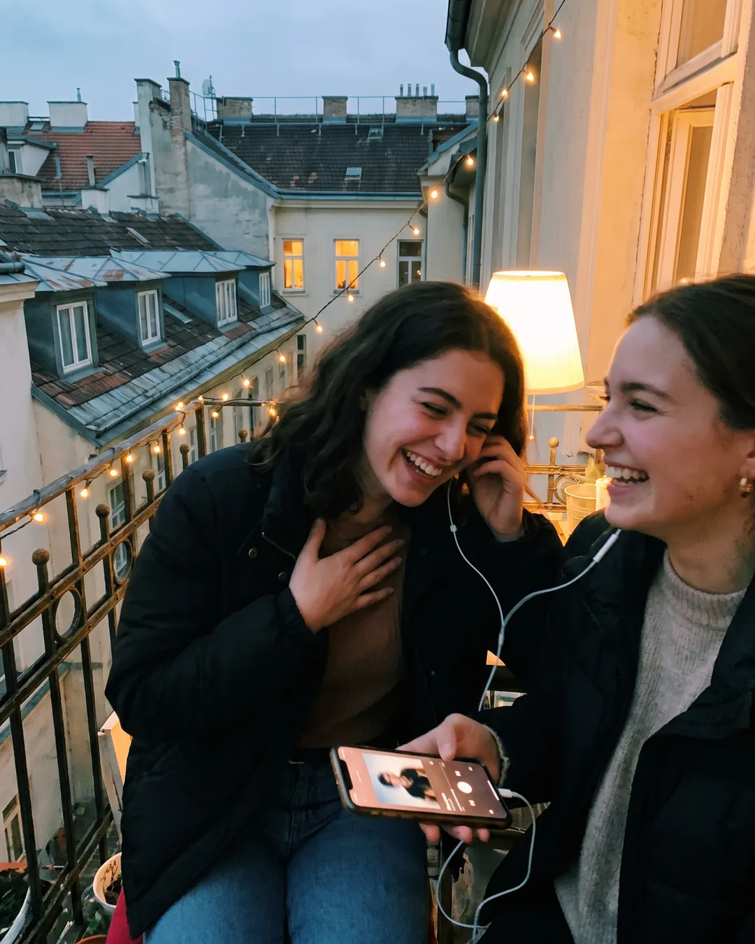 Zwei Freundinnen teilen sich Kopfhörer am Balkon in Wien